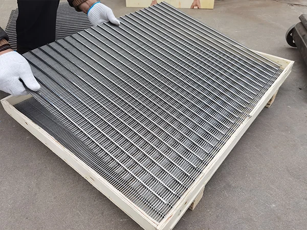 The worker is preparing to place a square wedge wire screen panel into a wooden crate.