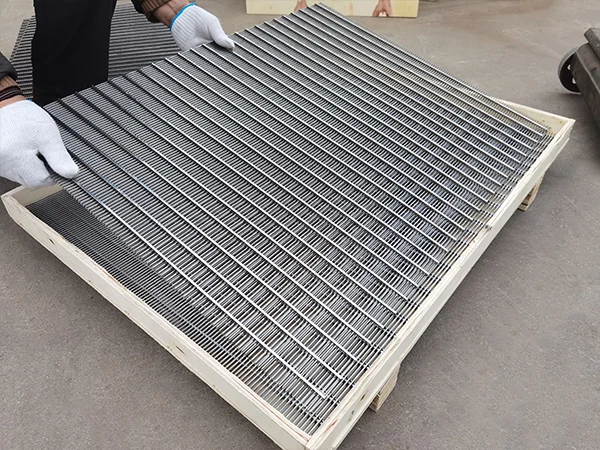 The worker is preparing to place a square wedge wire screen panel into a wooden crate.